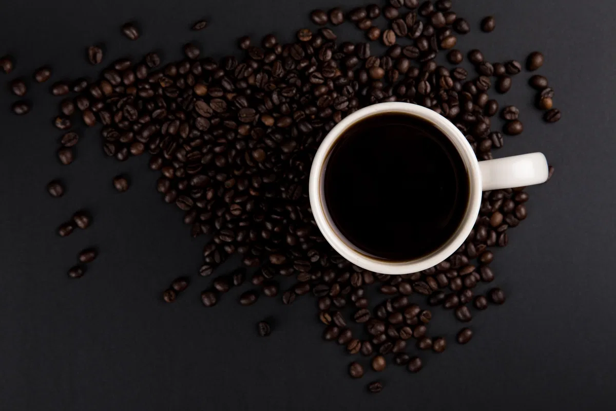A plain cup of coffee beside roasted coffee beans.