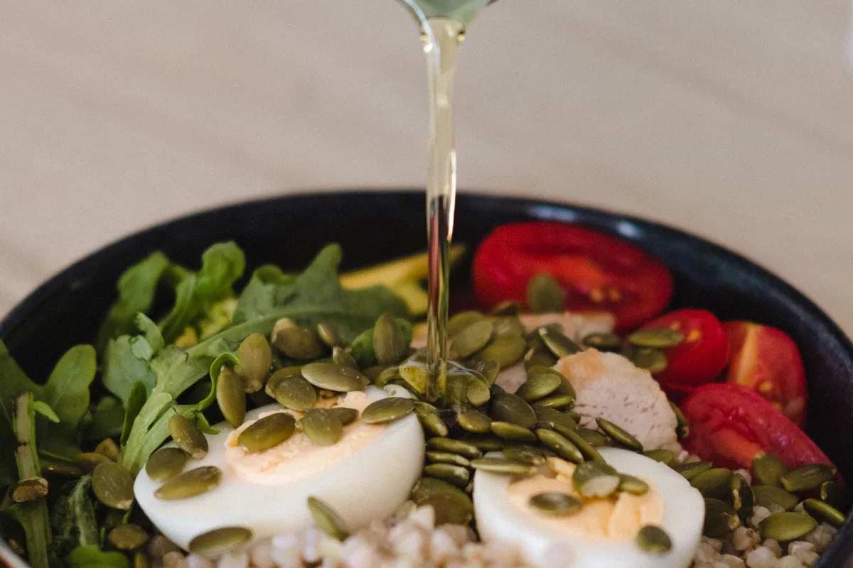 Olive oil being poured over a grain and vegetable bowl.