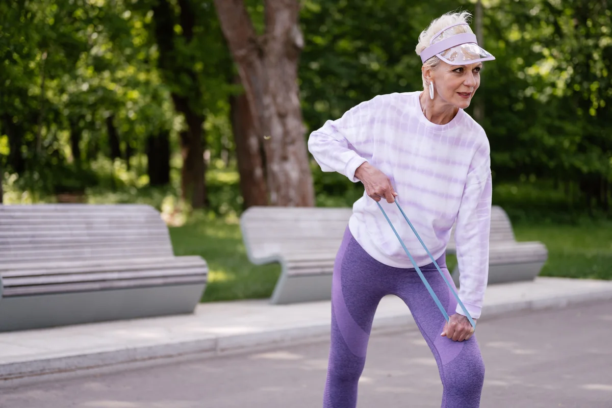 An adult exercising outdoors with a resistance band.