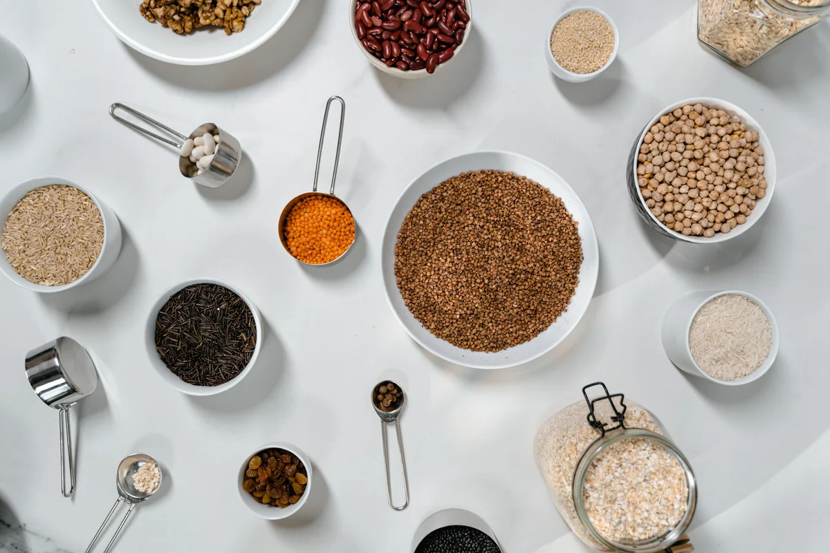 Bowls and jars of grains, beans, lentils and oats arranged on a table.