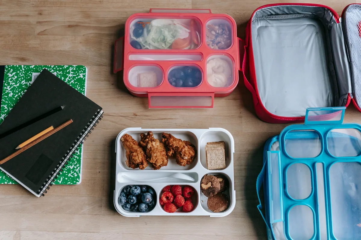 Prepared lunch boxes beside notebooks on a table.