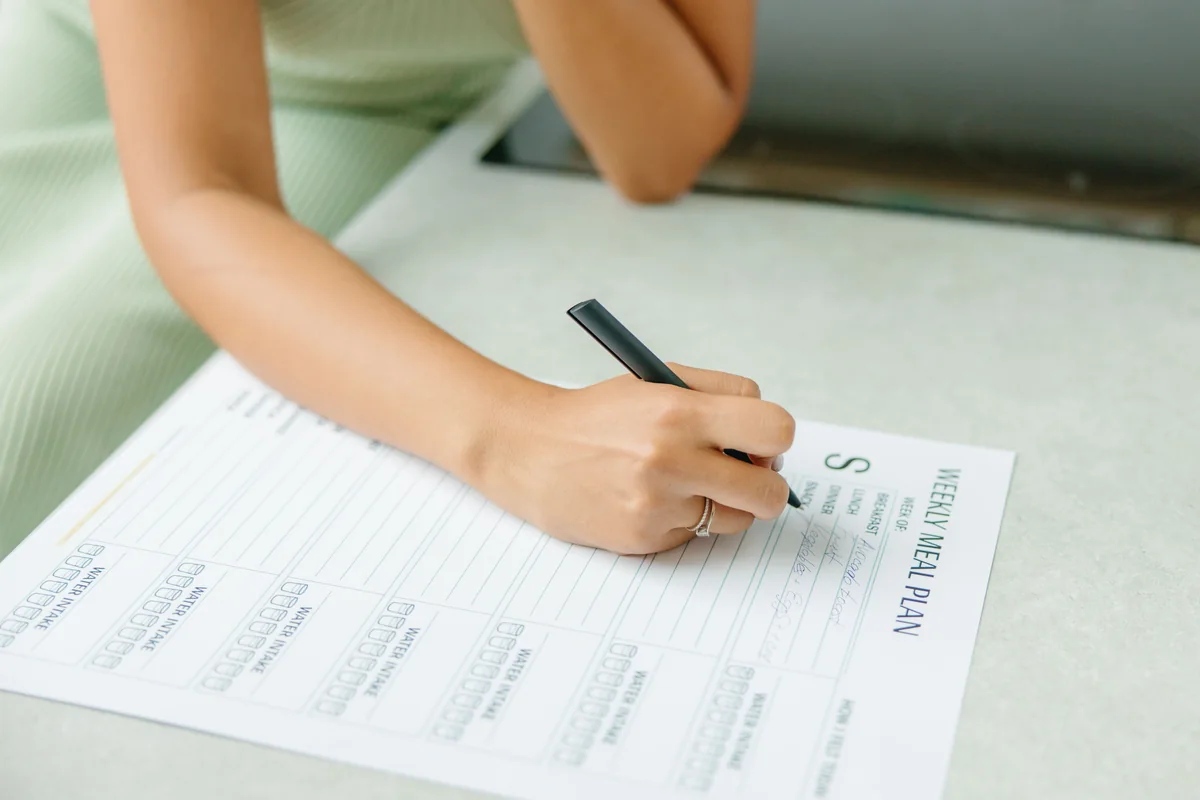 A weekly meal-planning worksheet being filled in at a kitchen table.