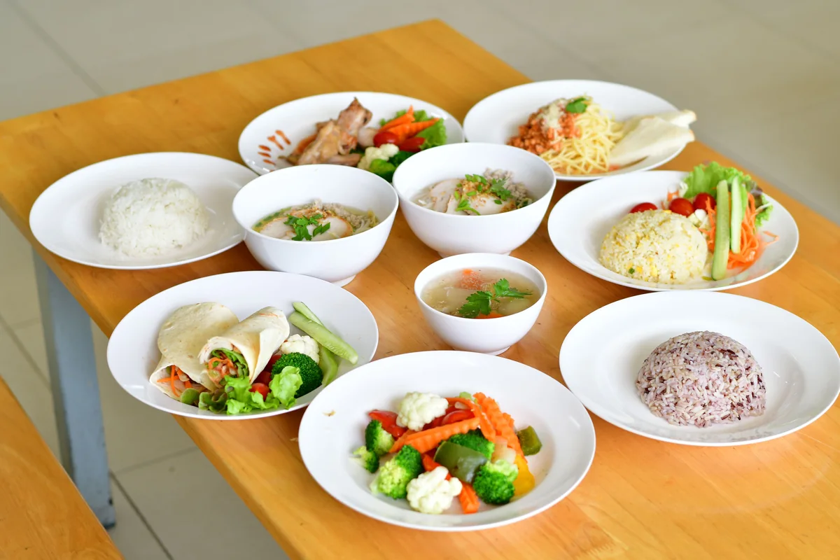 A table set with a variety of cooked dishes, rice, wraps and vegetables.