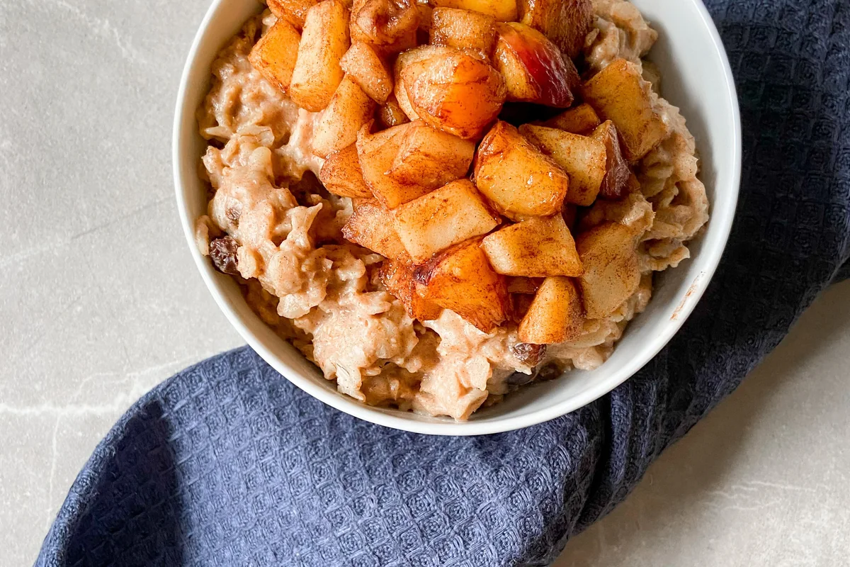 A bowl of porridge topped with cooked apple and cinnamon.