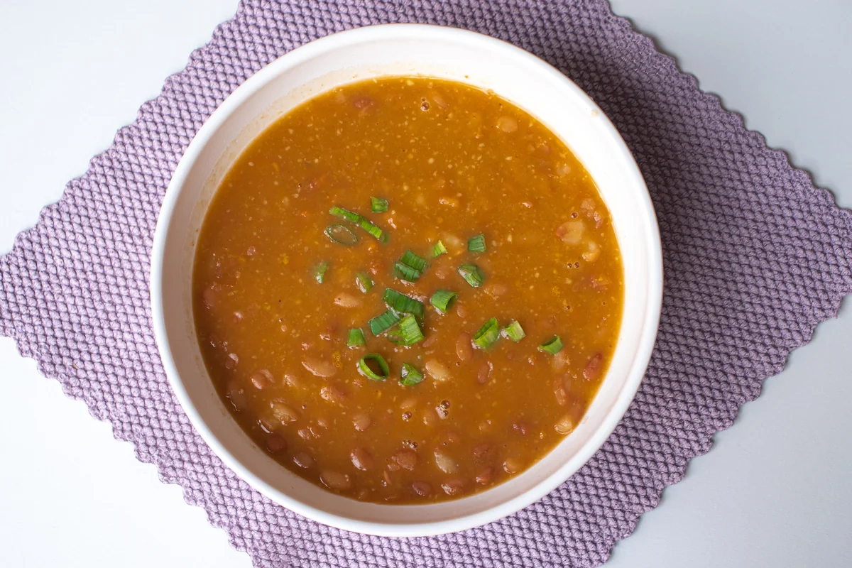 Hearty bean soup in a white bowl garnished with sliced spring onion