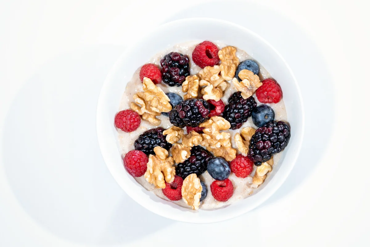 Overnight oats topped with mixed berries and walnuts in a white bowl.