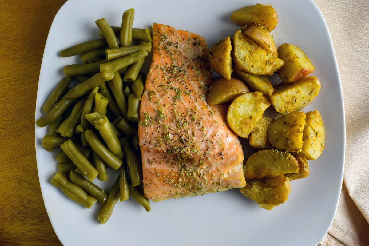 Cooked salmon served with roasted potatoes and green vegetables.