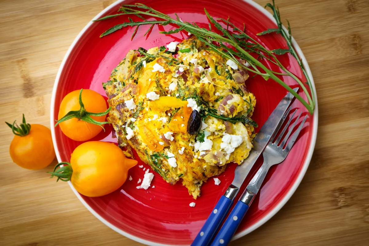An omelette with tomato, herbs and crumbled cheese on a red plate.