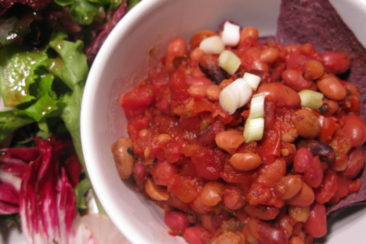 A tomato-based bean chilli served in a bowl with leafy salad alongside.