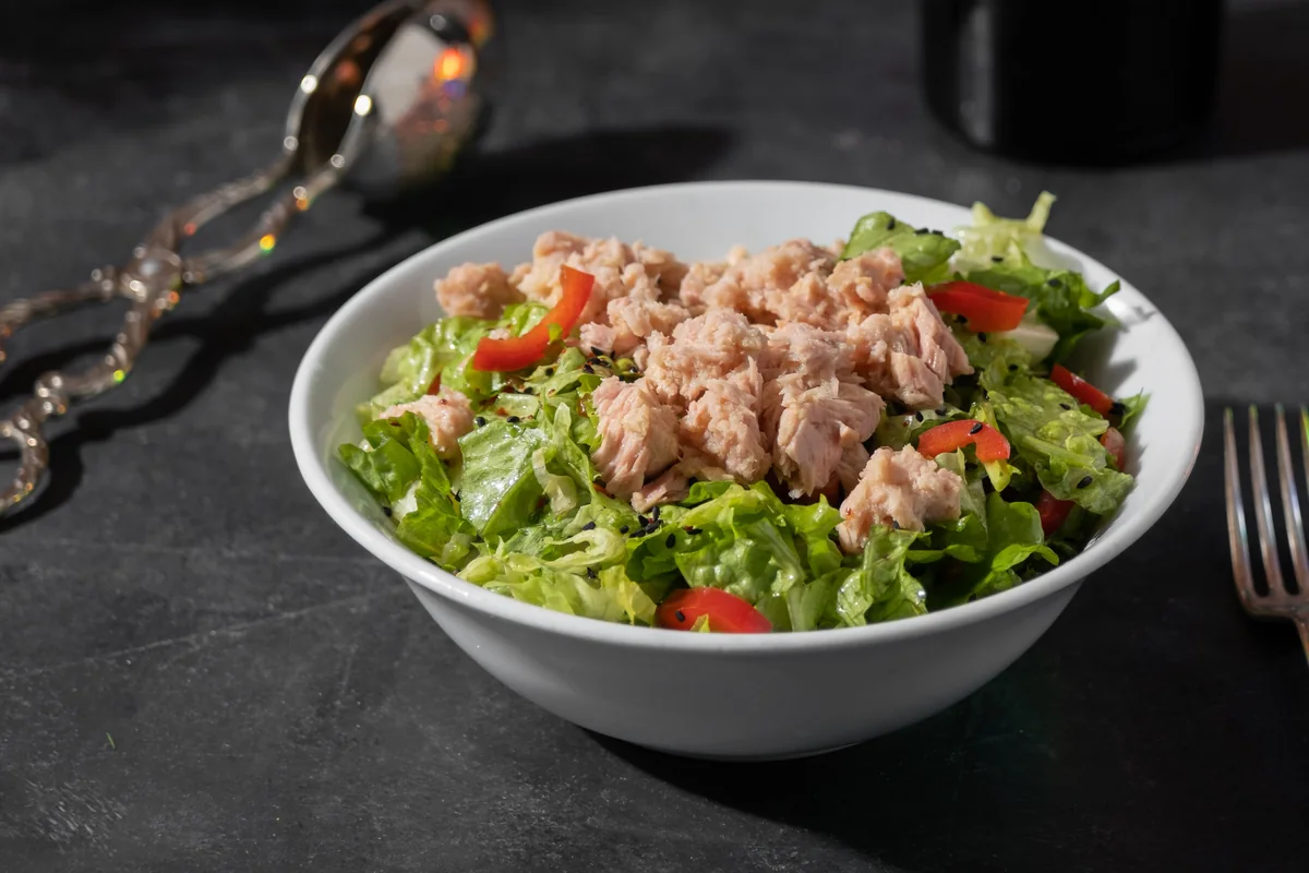 Tuna salad with fresh lettuce and red tomato pieces in a white bowl