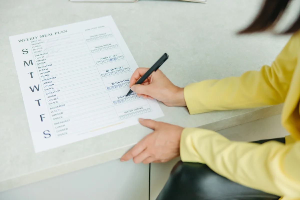 A person writing on a weekly meal-planning checklist.