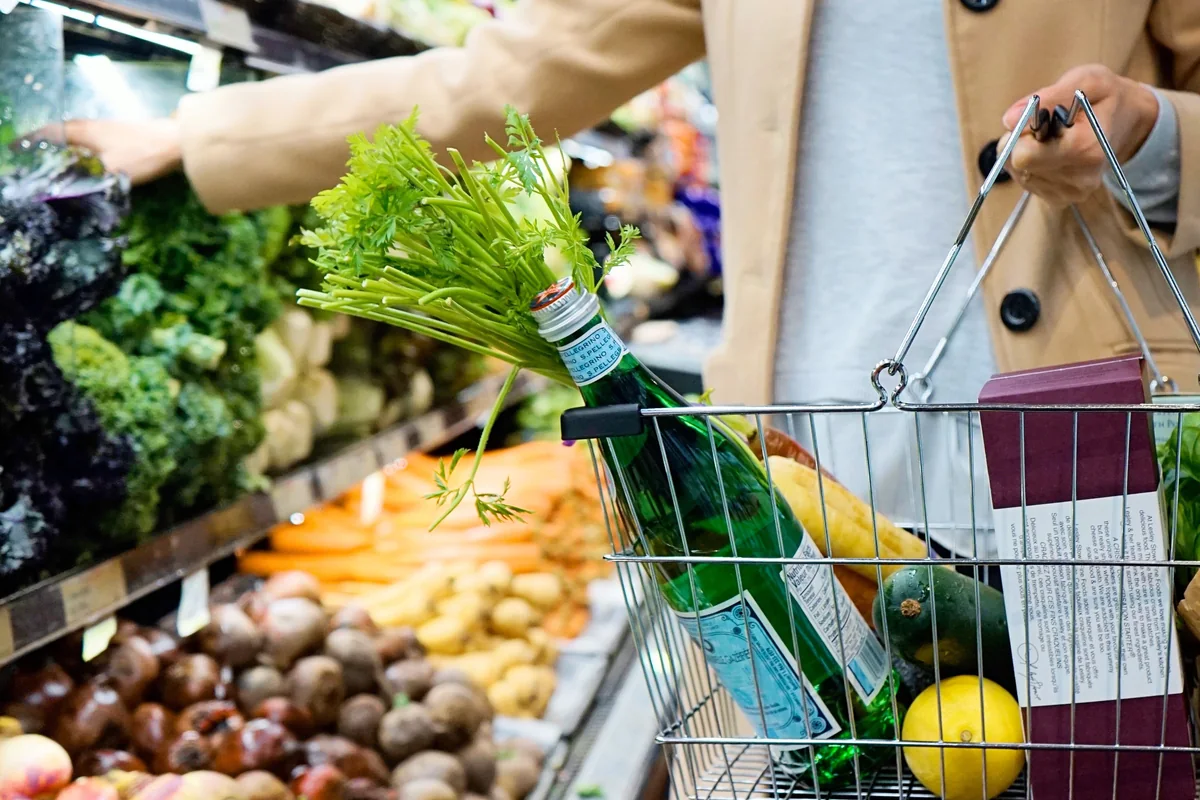 A shopper choosing fresh vegetables with a grocery basket.